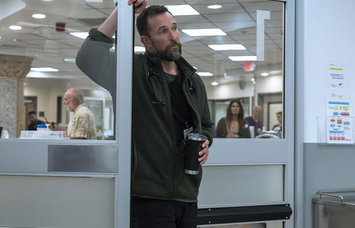 Man with stethoscope leaning on doorframe inside hospital corridor, scene from The Pitt Season 2 Episode 2 preview.