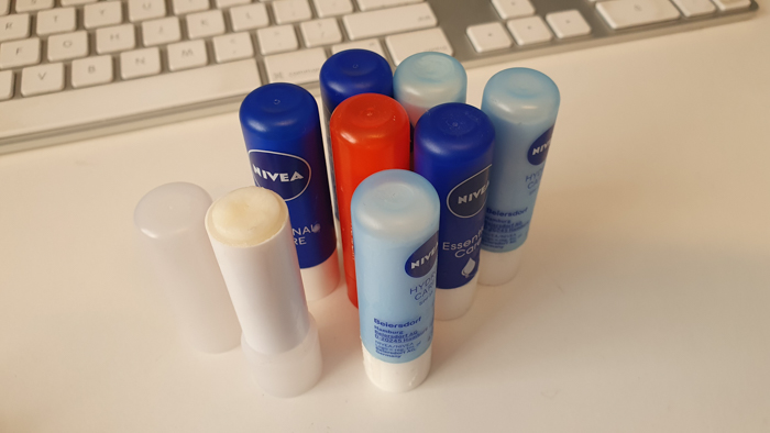 Several lip balm sticks arranged on a white surface near a computer keyboard, representing self-care resolutions.
