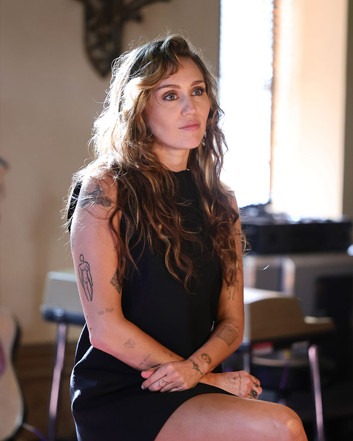 Young woman with tattoos sitting indoors, reflecting on nannies and the internet raising kids in modern parenting discussions