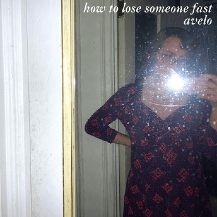 Person taking a mirror selfie with flash reflecting, wearing a patterned dress, featured on a hilariously bad album cover.