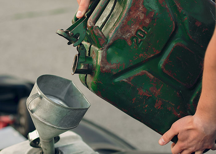Person pouring fuel from a rusty green gas can into a vehicle using a metal funnel, symbolizing a perfect revenge act.