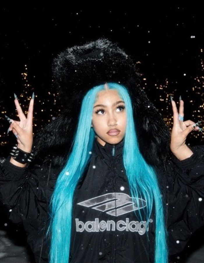 Young woman with long blue hair wearing a black Balenciaga jacket posing outdoors with snowflakes, evoking super cringe viral moments.
