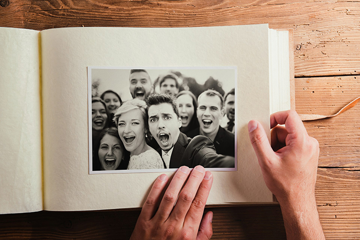 Hands holding a photo album with a black and white wedding group photo, highlighting bride and family drama moments.