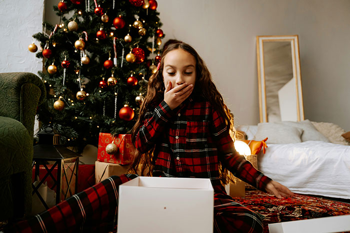 Young daughter in red pajamas surprised by Christmas presents under a decorated tree, highlighting gift imbalance with half-brother. Young daughter in red pajamas surprised by Christmas presents under a decorated tree, highlighting gift imbalance with half-brother.
