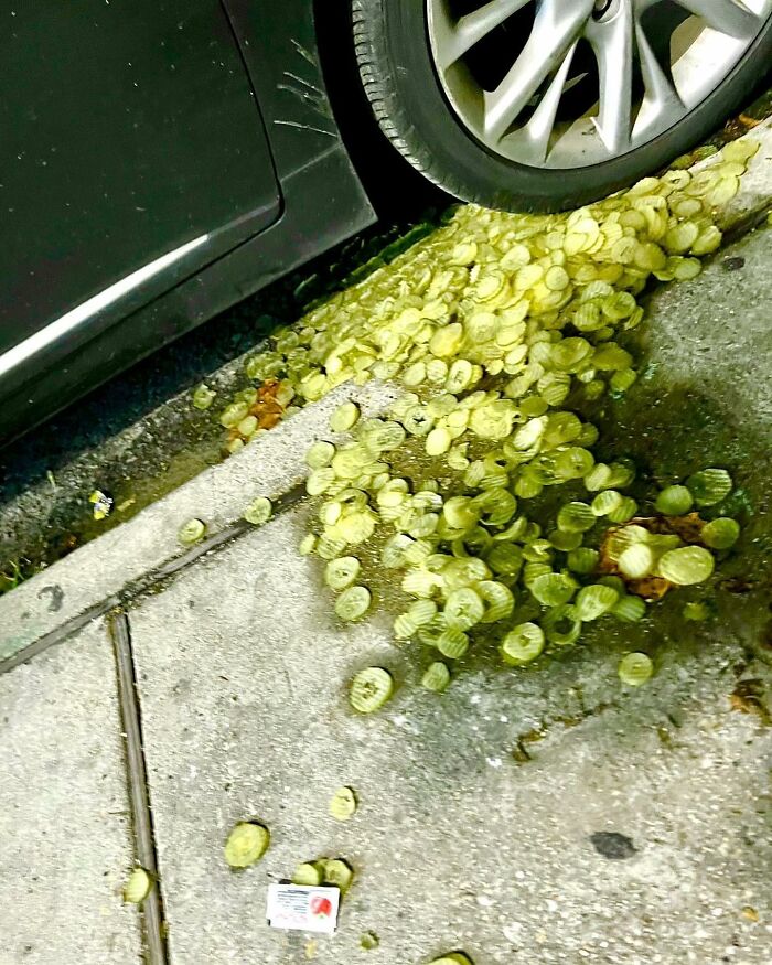 Car tire parked over a large pile of weird green street objects scattered on the sidewalk and curb.