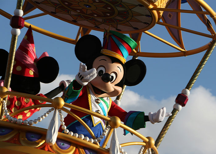 Mickey Mouse mascot waving from colorful parade float at Disney World under blue sky