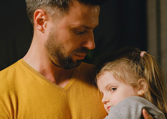 Man holding young girl closely, reflecting on life changes after learning he is not the biological parent.