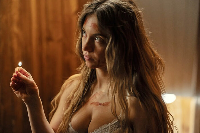 Woman in intimate photoshoot holding a lit match, wearing lace lingerie with chest scars and moody wooden background