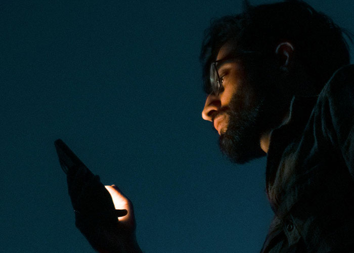 Person with glasses looking at a phone in the dark, illustrating habits neurodivergent people thought were normal.
