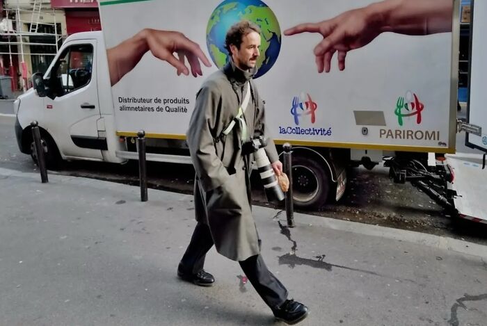 Man with camera walking past street art of hands reaching for globe, capturing life’s unexpected and beautiful street moments.