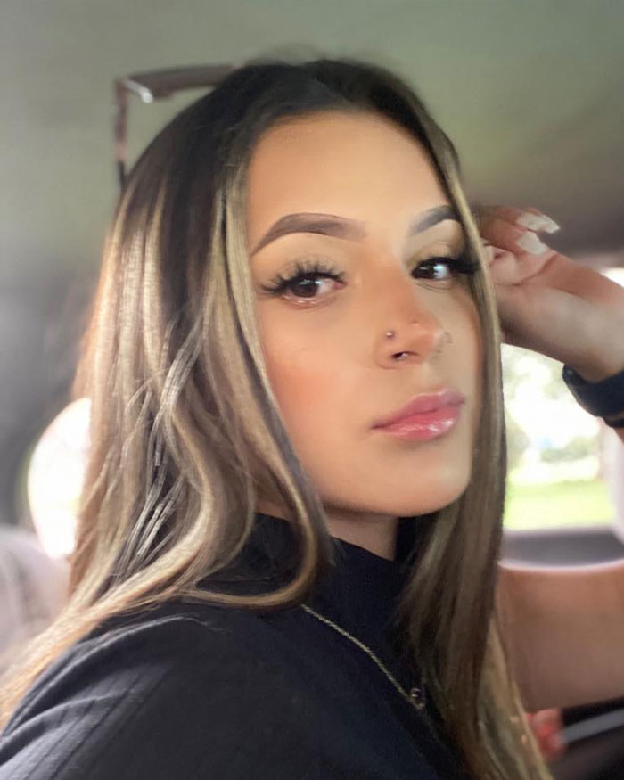 Young woman with long hair and nose piercing looking at camera inside a car, related to jealous girlfriend accused in gym fight.