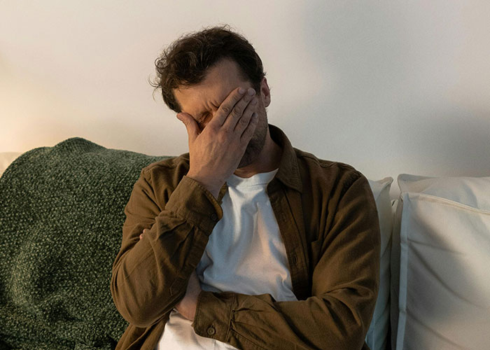 Man sitting on sofa with hand covering face, appearing distressed, illustrating regret after revenge acts.