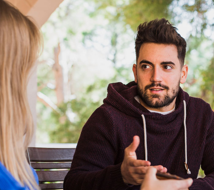 A man in a dark hoodie explaining something to a woman outdoors, highlighting signs that made sense after cheating came out.