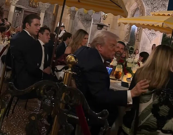 Melania Trump and guests at Mar-a-Lago, seated under yellow umbrellas during an evening event.