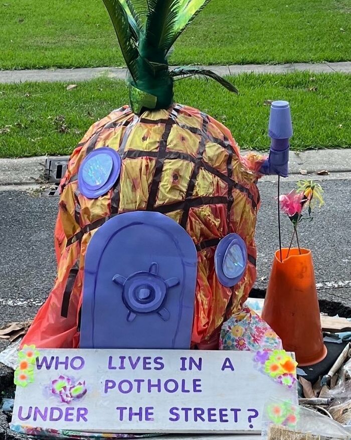 Decorative pineapple house art installation in a street pothole with a sign referencing weird street finds.