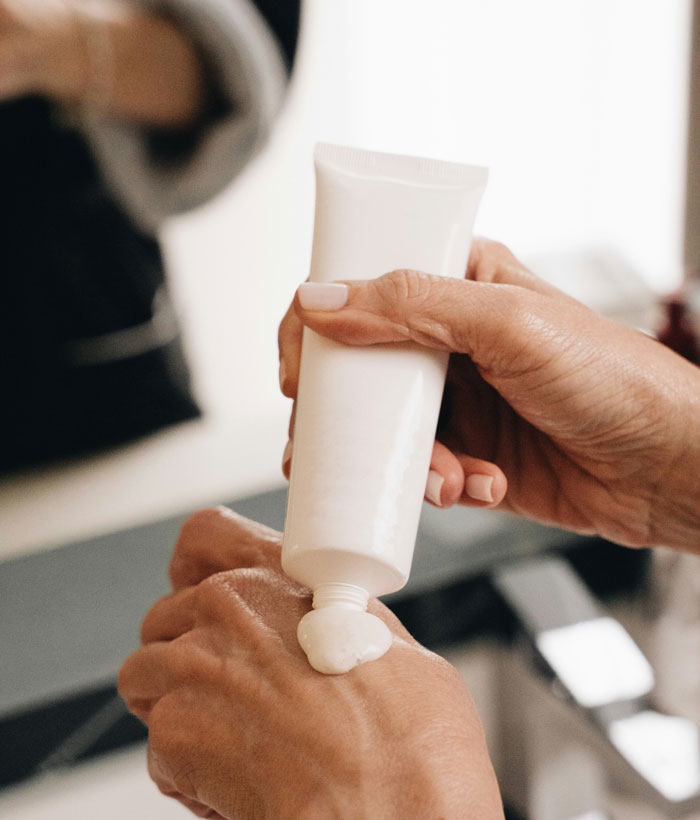 Hands applying lotion from a white tube on bathroom sink, friends family weird theme