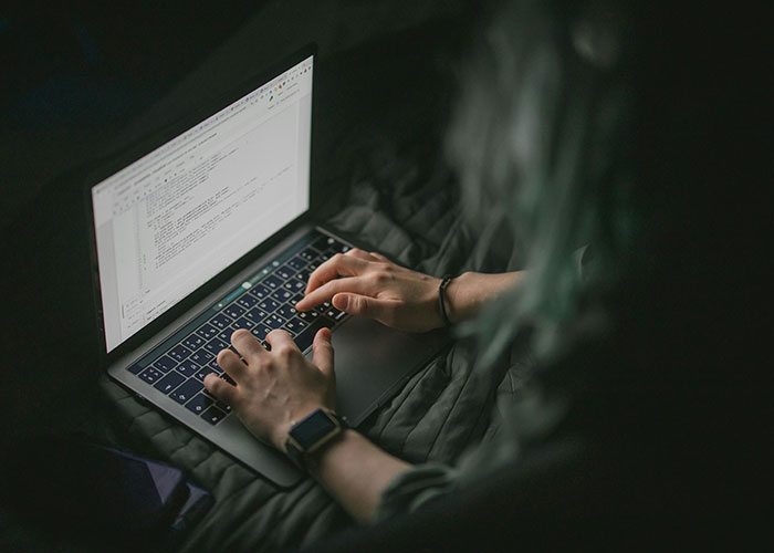 Person typing on a laptop in a dark setting, illustrating themes related to neurodivergent experiences and awareness.
