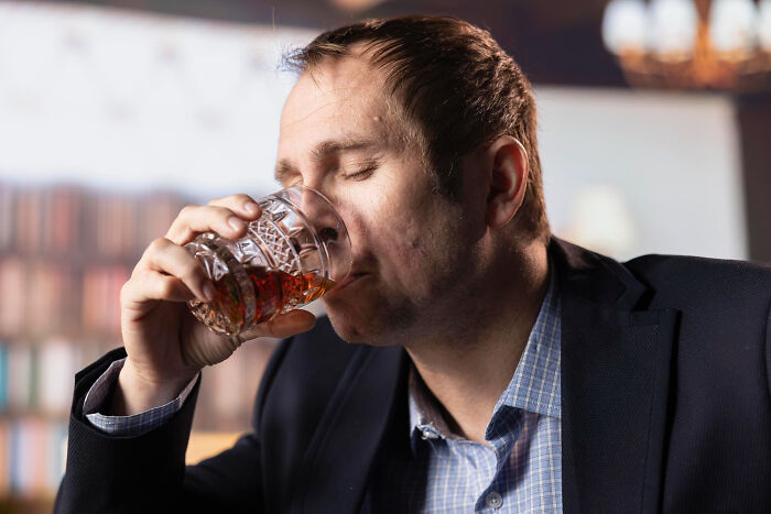 Man in a suit drinking whiskey, experiencing relatable moments that hit people harder than they’d like to admit.