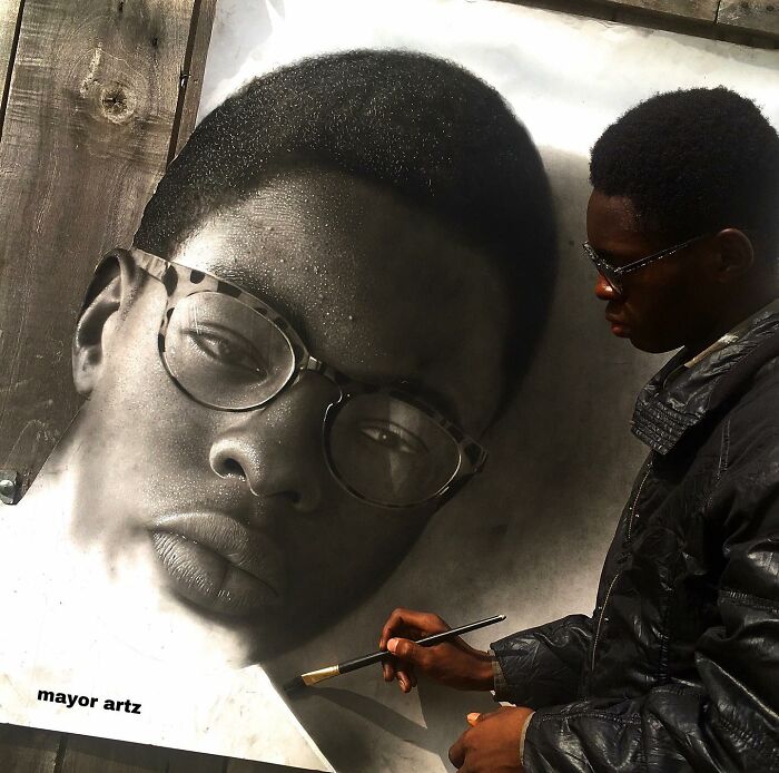 Artist creating hyperrealistic portrait painting of a man wearing glasses, showing behind-the-scenes drawing process.
