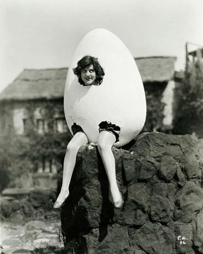 Woman posing inside a giant egg costume with legs sticking out, an odd and creepy old black and white photo.