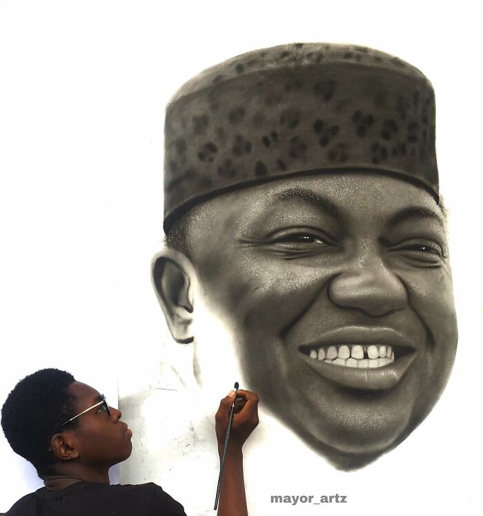 Artist creating a hyperrealistic portrait on a white wall, capturing detailed facial features with airbrush technique.