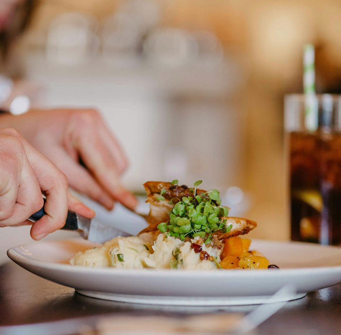 Hands cutting a plated meal with mashed potatoes and microgreens, friends or family were very weird