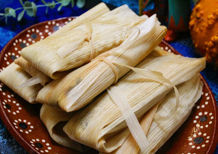 Stack of traditional Mexican tamales wrapped in corn husks on a decorative plate, fun facts about Mexico.