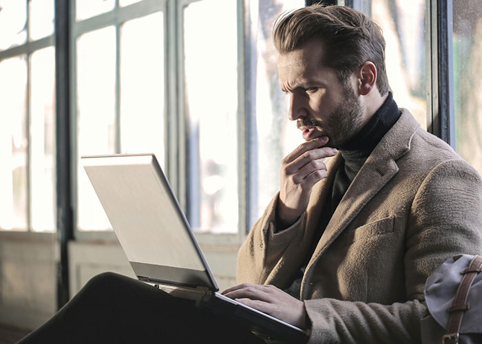 Man in a brown coat using a laptop, deep in thought, illustrating neurodivergent habits considered normal.
