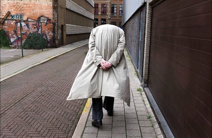 Person walking in a narrow urban alleyway wearing a beige trench coat capturing a street photo moment.