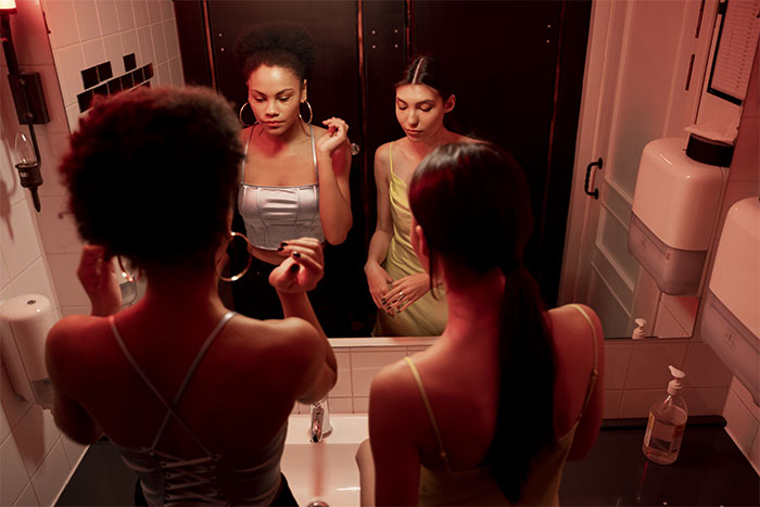 Two women getting ready in a nightclub bathroom mirror, capturing the essence of crazy party stories and nightclub vibes.