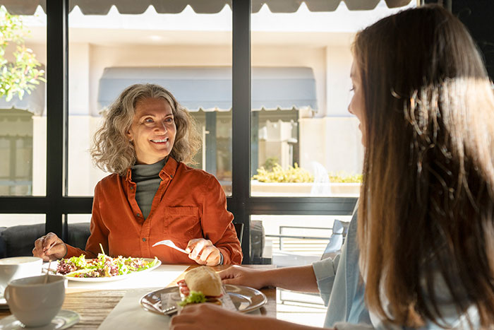 Middle-aged woman and younger woman having lunch, illustrating MIL tries to turn DIL pregnancy emergency into Facebook likes concept.