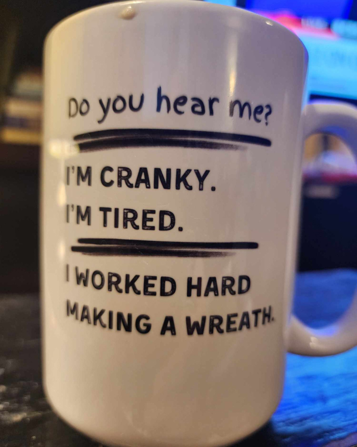White coffee mug with black text saying cranky, tired, and hard work, reflecting humor for people who hate New Year's resolutions.