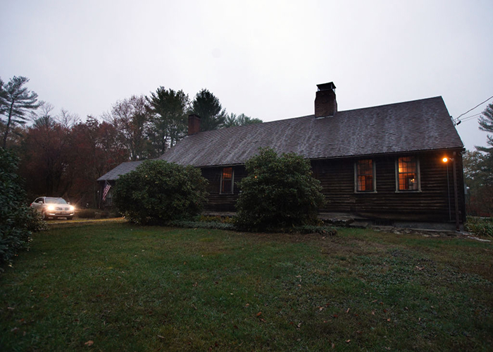 Old dark house at dusk with lit windows and a car approaching, representing haunted places in America.