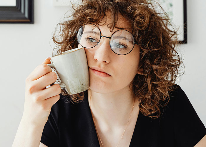 Young woman with curly hair and glasses looks thoughtful while holding a mug, reflecting on being neurodivergent.