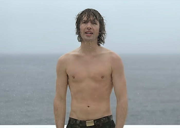 Shirtless man with wet hair standing by the ocean, illustrating hidden stories in famous songs transforming how you hear them.