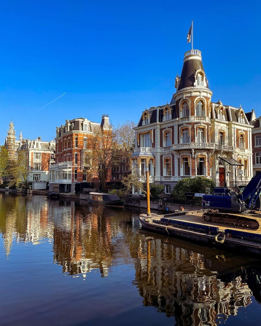 Historic European buildings reflecting on calm canal water under clear blue sky, a top place you should visit.