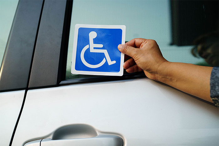Person placing a disabled parking permit sticker on a car window to indicate a disability permit.