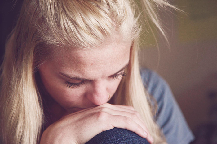 Woman with blonde hair looking down, resting her head on her hand, reflecting on wife husband life decision.
