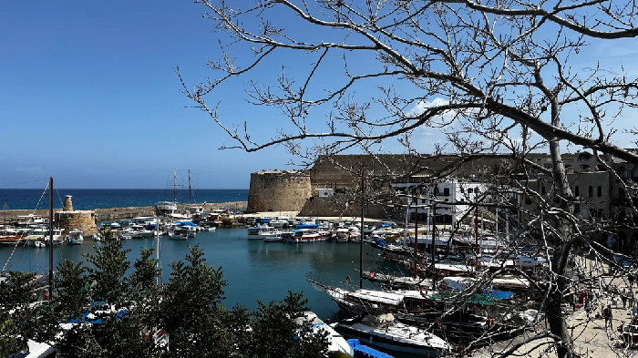 Harbor with boats, stone fort and bare tree branches under clear blue sky, photo for Most Stressful Countries feature