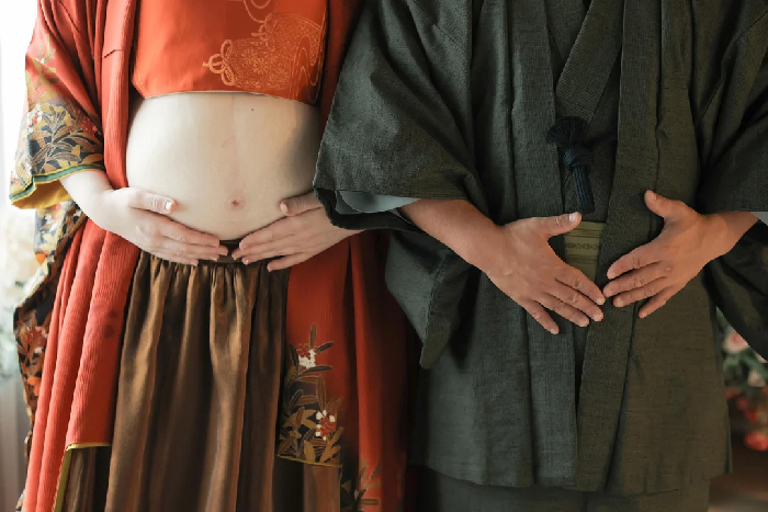 Pregnant person and partner in kimonos with hands framing exposed belly, maternity photoshoot
