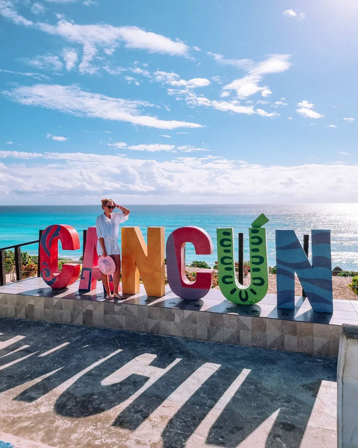 Woman posing with colorful CANCÚN sign on turquoise beach, illustrating fun facts about Mexico and coastal travel
