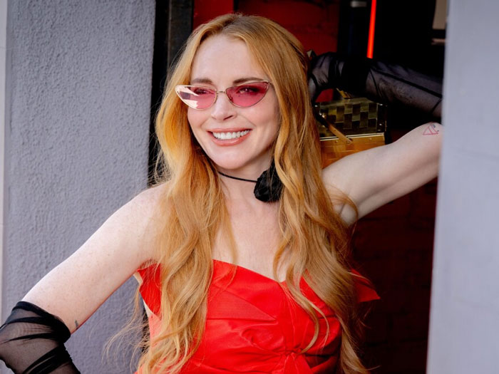 Smiling woman with long red hair and pink sunglasses wearing a red dress, representing celebrities whose careers crashed.