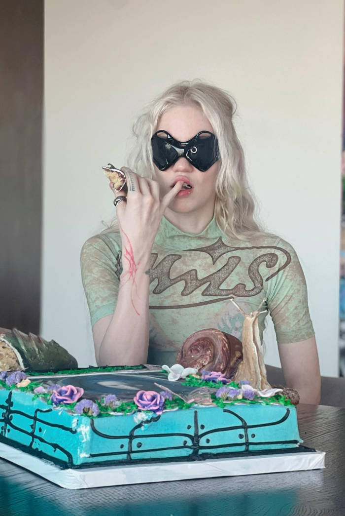 Person with blonde hair and unique black sunglasses sitting behind a decorated cake, representing Elon Musk&rsquo;s children topic.