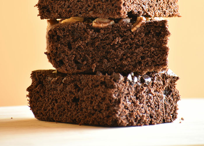Stack of three moist chocolate brownies with nuts on a light surface illustrating perfect revenge acts concept.