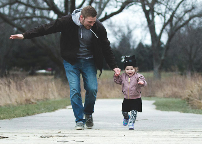 Man and young girl holding hands and walking outdoors illustrating men sharing how lives changed after discovering they aren’t biological parent.