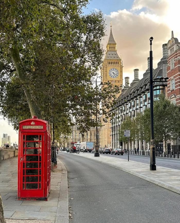 Red phone booth by a quiet London street with Big Ben in the background, representing countries that sleep the most.