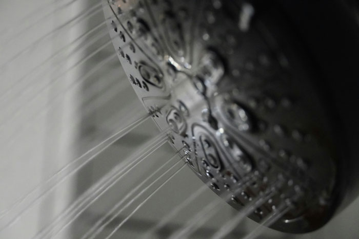 Close-up of a showerhead with water flowing, illustrating privacy and secrecy linked to phone and cheating topics.