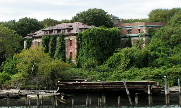 Abandoned building overgrown with vines surrounded by dense greenery near a broken dock in a forbidden place on Earth.