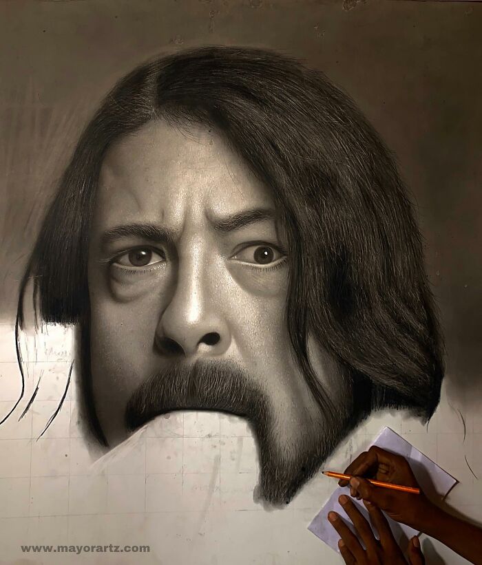 Hyperrealistic portrait in progress showing detailed facial features and hair, with artist’s hand drawing on paper.