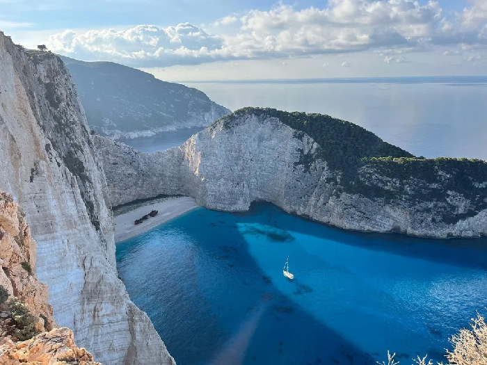 Most Stressful Countries concept: dramatic white cliffs, turquoise bay with a small sailboat and sandy beach.
